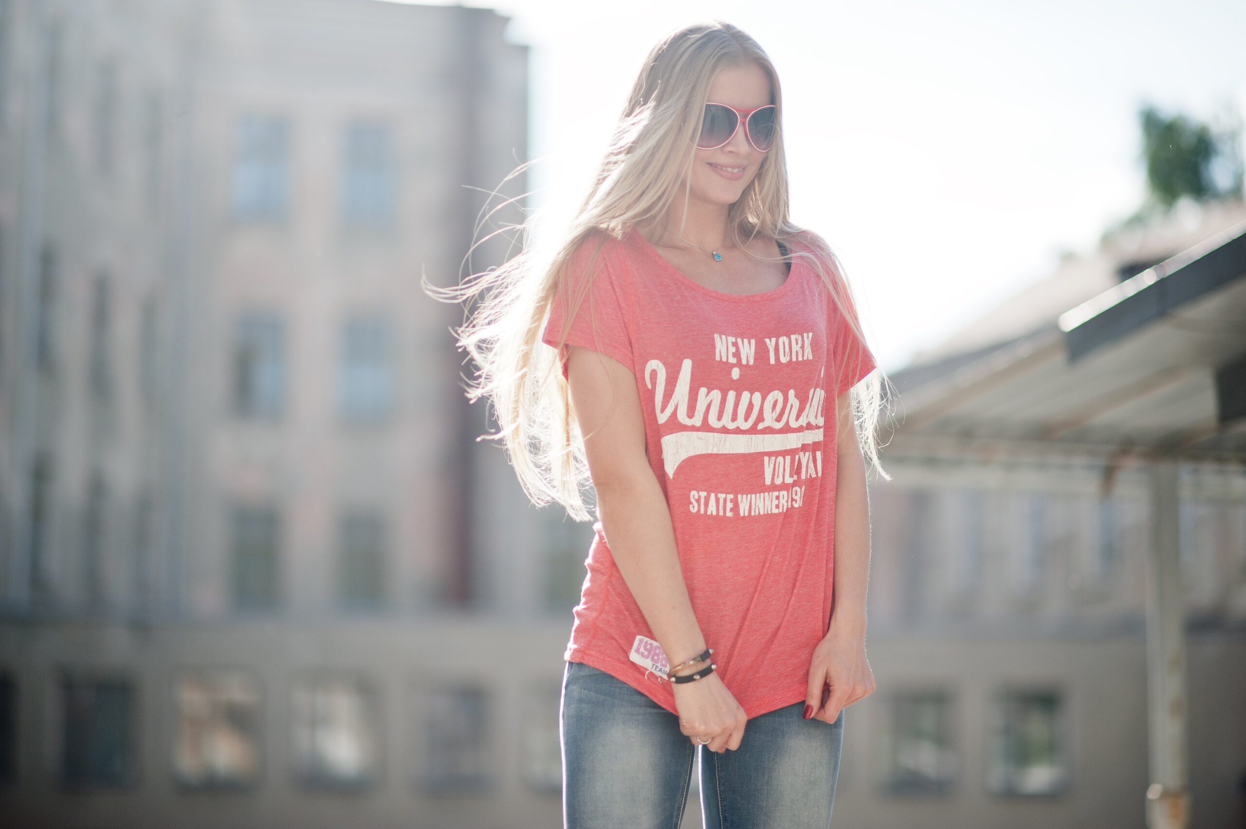 Stylish happy blonde woman wear at jeans, sunglasses and t-shirt posed at street on sunny weather. Fashion urban model portrait.